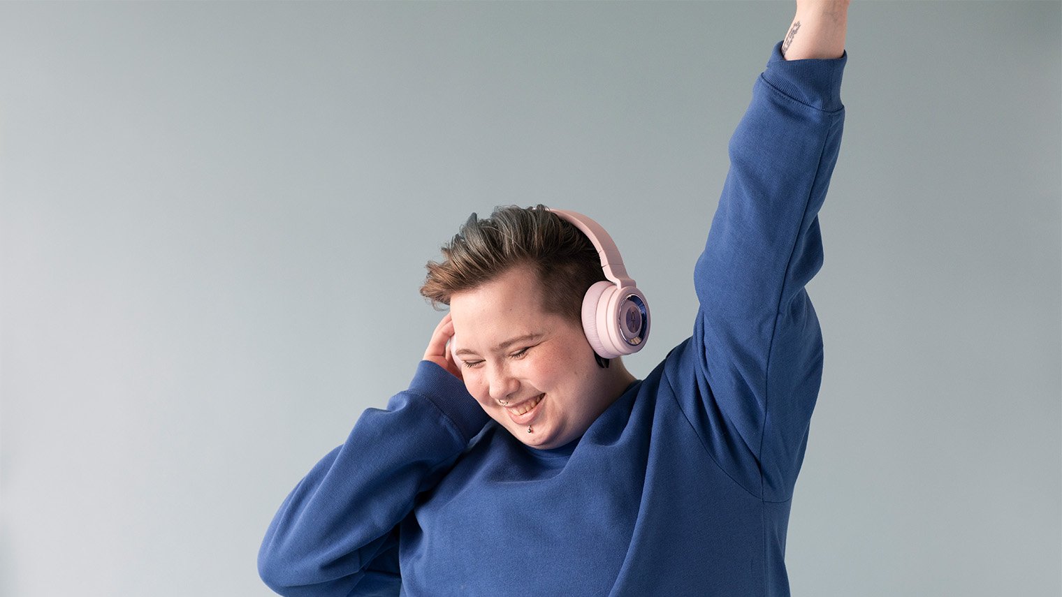 Nuori henkilö fiilistelee musiikkia vaaleanpunaiset kuulokkeet korvillaan. 